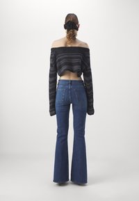 Mustavalkoraidallinen lyhyt neule, jossa on olkapäät paljastava malli, yhdistettynä sinisiin leveneviin farkkuihin, joissa on takataskut ja kulutustiedot.