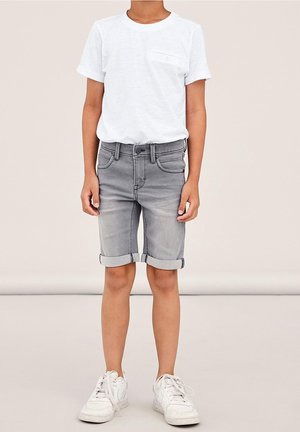 White short-sleeve t-shirt with a chest pocket, paired with light gray denim shorts featuring rolled cuffs and five pockets. White sneakers.