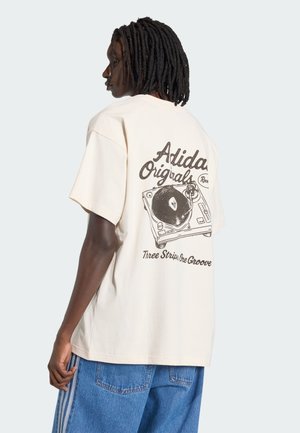 Beige cotton t-shirt with a relaxed fit, featuring a black graphic of a turntable and text on the back, short sleeves, and a round neckline.