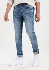 Jeans in denim blu chiaro con un design sbiadito, taglio affusolato e risvolti. Abbinati a sneakers bianche e a un dolcevita grigio chiaro.