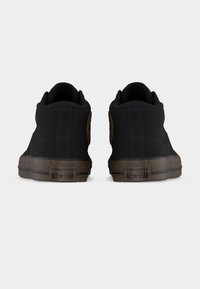 Mustade Converse All Star keskmise kõrgusega tossude paar, nähtud tagantpoolt, millel pruunid tallad ja mustad logomärgid.