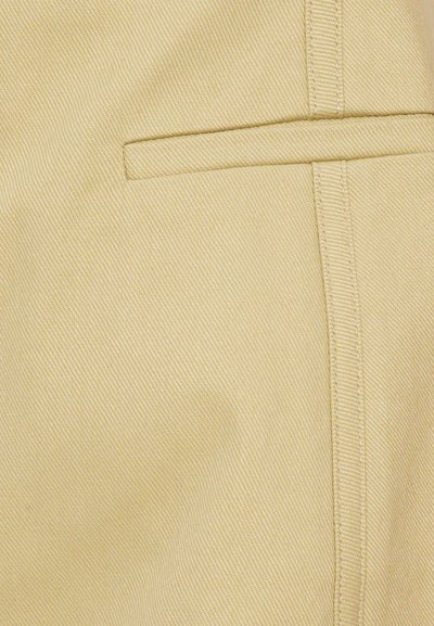 Pantaloni bej dintr-un material texturat, cu un buzunar lateral discret, cusături vizibile și un design croit.