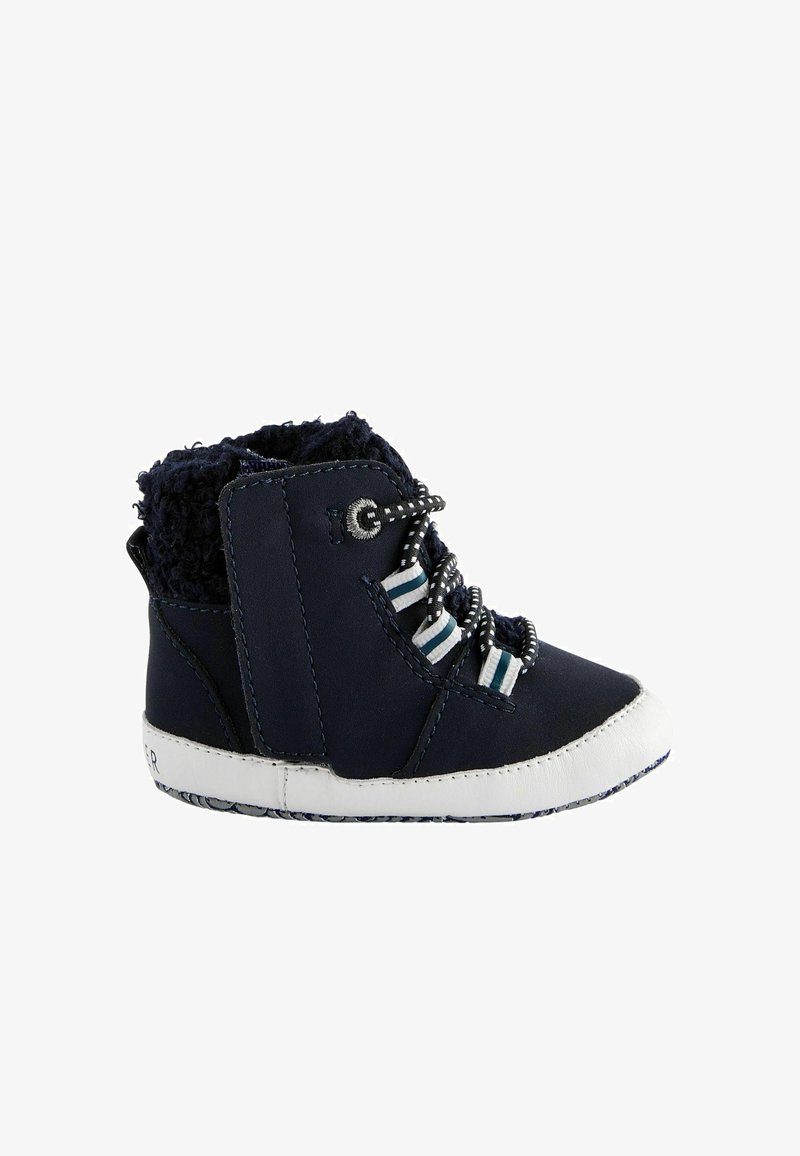 Sötétkék bőr csizma fehér gumitalppal. Részletei között szerepel a bolyhos bélés, csíkos fűzők és ezüst színű kiegészítők. Közepes magasságú dizájn.