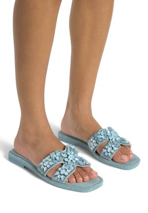 Ciabatte in blu chiaro caratterizzate da un materiale scamosciato testurizzato, decorate con gemme luccicanti di diverse dimensioni disposte in un motivo floreale lungo le cinghie.