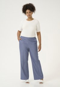 Pantaloni larghi a righe blu con una texture liscia, abbinati a un top aderente bianco a maniche corte. La modella sta in piedi con sicurezza.