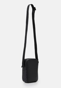 Borsa a tracolla nera con forma rettangolare, materiale in pelle, chiusura con zip e una tracolla regolabile con branding impresso.