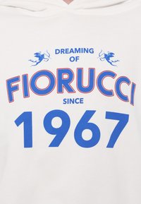 Hvit hettegenser med stor blå tekst som sier "DREAMING OF FIORUCCI" og "1967", samt en liten blå grafikk av en figur og en sløyfe.
