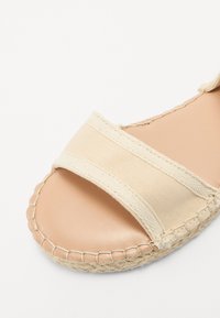 Sandale espadrille beige avec deux sangles en toile, bords cousus, semelle intérieure en cuir lisse et détails en jute tressé le long de la semelle.
