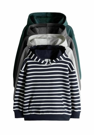 Barn med bølget hår iført en sort-hvidstribet hættetrøje, der trækker hætten op, iført blå jeans, neutralt baggrund.