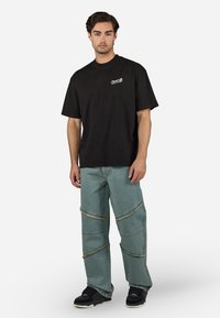Sort bomulds T-shirt med korte ærmer og et lille grafisk motiv foran, parret med lyseblå denimbukser med slidte detaljer og løs pasform.