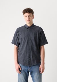 Πουκάμισο κοντομάνικο με γιακά σε ναυτι�κό μπλε με λευκό καρό σχέδιο. Έχει χαλαρή εφαρμογή και λεία υφή, συνδυασμένο με ανοιχτό μπλε τζιν.