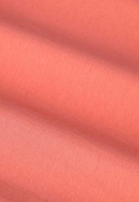 Tissu en coton d'une douce couleur corail, avec une texture lisse présentant des motifs de tissage subtils et de légers plis.