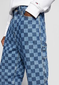 Modré kostkované džíny mají mix světle a tmavě modrých čtverců, boční kapsy a klasický design pasu.