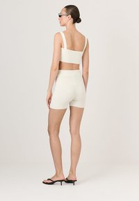Heledbeige ribakujuline lühike top ja sobivad kõrge vöökohaga lühikesed püksid, kombineeritud mustade kontsakingadega. Sujuv tekstuur, minimalistlik disain.