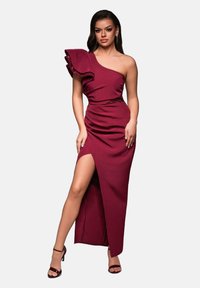 Robe bordeaux à une épaule avec accent en volants, design froncé, fente haute et ceinture texturée, portée avec des talons à lanières.