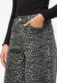 Pantalon imprimé léopard en gris et noir, avec une poche avant et un bouton argenté, fabriqué en tissu texturé avec une coupe à jambes larges.