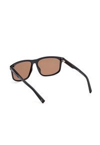 Schwarze Sonnenbrille mit einem rechteckigen Rahmen, braun getönten Gläsern, dünnen Bügeln und einer strukturierten Oberfläche am Bügel für zusätzlichen Komfort.