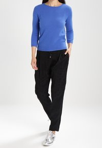 Blå långärmad tröja i kombination med svarta strukturerade byxor. Modellen bär silverfärgade sneakers. Outfiten har en avslappnad och modern design.