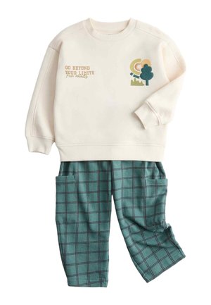 Kremowa bluza z nadrukiem "Przekraczaj swoje granice" i grafiką drzewa. Zielone spodnie w kratę z kieszeniami i elastycznym paskiem w talii. Miękki materiał.