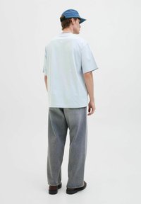 Hellblaue Baumwoll-T-Shirt mit kurzen Ärmeln, kombiniert mit lockeren grauen Denim-Hosen. Verfügt über ein Logo-Detail auf dem Rücken und ein minimalistisches Design.