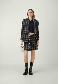 Zwart-witte geruite blazer met bijpassende rok. Kenmerkt zich door grote knopen, een cropped top en zwarte kniehoge laarzen. Glad stoftextuur.