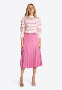 Falda rosa con pliegues de tejido texturizado, combinada con una blusa de rayas blanca y rosa de manga larga. Sandalias plateadas completan el conjunto.