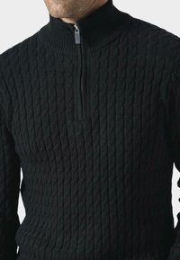Czarny dziany sweter z wysokim kołnierzem i ćwierć zamkiem. Posiada teksturowany wzór w warkocze, zapewniający dopasowane fason i ściągacze.