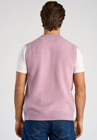 Hellrosa gestrickte Weste mit geripptem Ausschnitt und Saum, die eine glatte Textur aufweist. Trägt man über einem weißen T-Shirt, kombiniert mit dunklen Jeans.