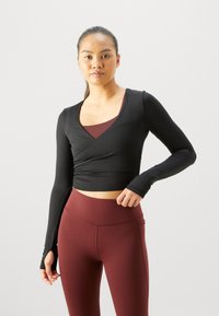 Zwarte cropped top met lange mouwen, een V-hals en een wikkelontwerp, gecombineerd met hoogwaardige bordeauxrode leggings met een gladde textuur.