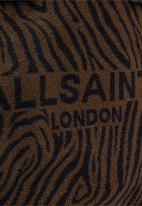 Hnědá látka s černým zebrovaným vzorem, s nápisem "ALLSAINTS LONDON" výrazně zobrazeným. Měkká textura a výrazný design.