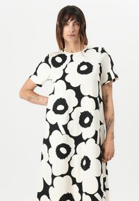 Lyhythihainen mekko, jossa on valkoinen kangas suurella mustalla kukkakuviolla, rento malli ja pyöreä kaula-aukko. Sileä rakenne.