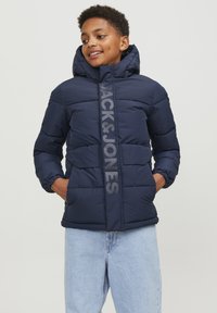 Mörkblå pufferjacka med hög krage, dragkedjestängning och "JACK&JONES"-logotyp fram. Har elastiska ärmavslut och en mjuk textur.
