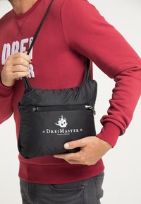 Schwarze Nylon-Umhängetasche mit einer vorderen Reißverschlusstasche und bedrucktem Logo. Leichtes Design mit verstellbaren Riemen.