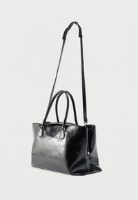 Μαύρη δερμάτινη τσάντα χειρός με διπλές κορυφαίες λαβές και ρυθμιζόμενο μακρύ λουρί ώμου, σε όρθια θέση πάνω σε απλό φόντο.