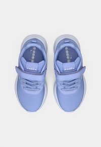 Baskets de sport violettes claires avec une tige en tissu texturé, des lacets élastiques et une sangle velcro sur le dessus du pied. Semelle blanche douce.