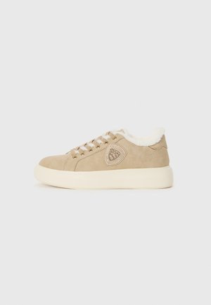 Beige suède sneaker met een pluizige witte binnenkant. Rond teen, textuuraccenten en beige veters. Licht verhoogde witte zool.