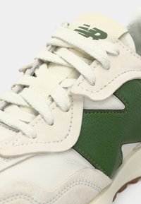 White and green sneaker featuring a textured leather and suede upper, with prominent stitching and a cushioned tongue. Lace-up design.