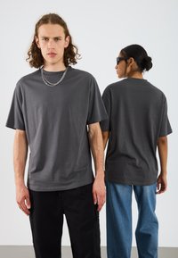 Graues T-Shirt mit kurzen Ärmeln in lässiger Passform, mit rundem Halsausschnitt, kombiniert mit schwarzen Hosen und blauen Jeans, mit silbernem Kettendetail.