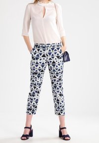 Lätt, semitransparent vit blus med volangkrage, kombinerad med mönstrade marinblå byxor med geometriska trianglar och ankelremmar.