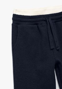 Pantalones jogger de textura de waffles en azul marino con una cinturilla elástica crema, cordón ajustable y bolsillos laterales. Vista en primer plano de la tela y detalles.