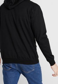 Felpa nera con cappuccio, maniche lunghe e una consistenza morbida. Abbinata a jeans in denim blu.