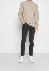 Beige svetr z ribovaného úpletu s kulatým výstřihem, kombinovaný s tmavými slim-fit džíny a bílými teniskami s minimálními detaily.
