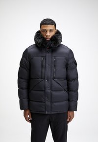 Svart boblejakke med pelsforet krage, glidelåslommer, quiltet design og frontknapplukking. Ensfarget, glatt materiale.
