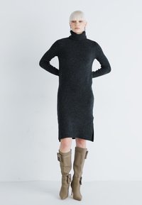 Dark gray knitted turtleneck dress with side slits, paired with knee-high taupe boots featuring buckle accents. Smooth texture throughout.