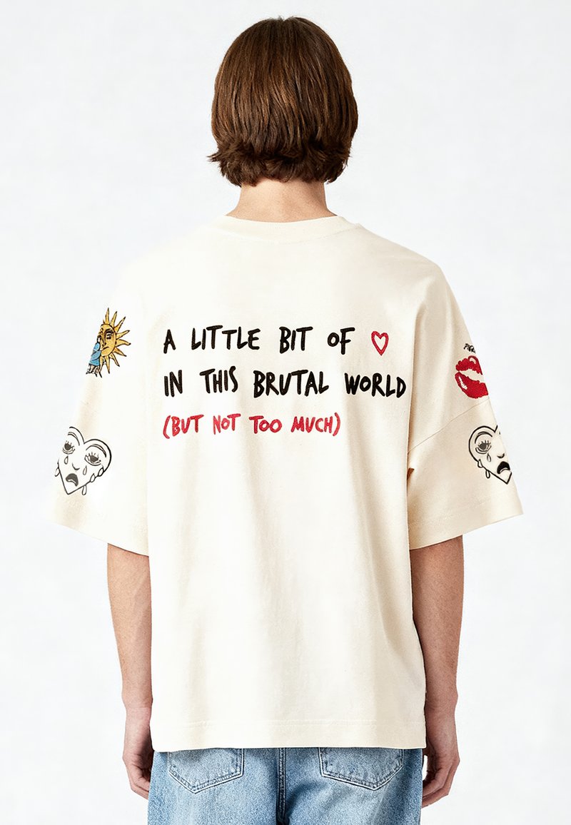 Krēmveida kokvilnas T-krekls ar pārspīlētu piegriezumu, kas ietver krāsainus grafiskos zīmējumus, uzsvērti tekstus un dizainus uz aizmugures un piedurknēm.