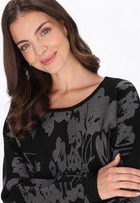 Pullover nero in maglia con un motivo floreale argentato, scollatura ampia a barca, maniche lunghe e polsini neri testurizzati.