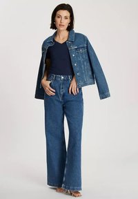 Dżinsowa kurtka z pasującymi szerokimi spodniami dżinsowymi w średnim niebieskim odcieniu, z klasycznym krojem, frontowymi kieszeniami oraz granatową koszulką typu v-neck pod spodem.