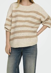 Béžový a krémový pruhovaný svetr s volným střihem, žebrovaným lemem a širokými rukávy, nošený přes světle modré, vybledlé široké kalhoty.