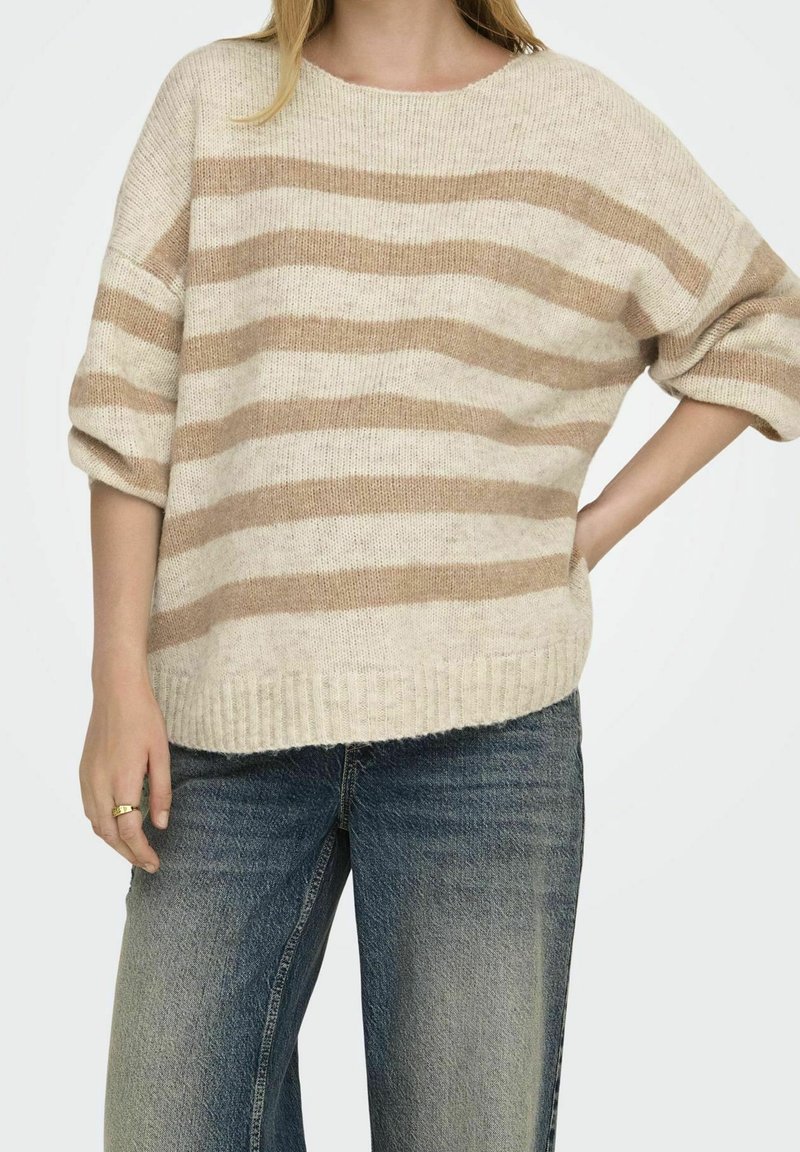 Béžový a krémový pruhovaný svetr s volným střihem, žebrovaným lemem a širokými rukávy, nošený přes světle modré, vybledlé široké kalhoty.
