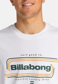 White short-sleeve t-shirt featuring a colorful graphic design with green, orange, and yellow stripes and "Billabong" text in bold green.